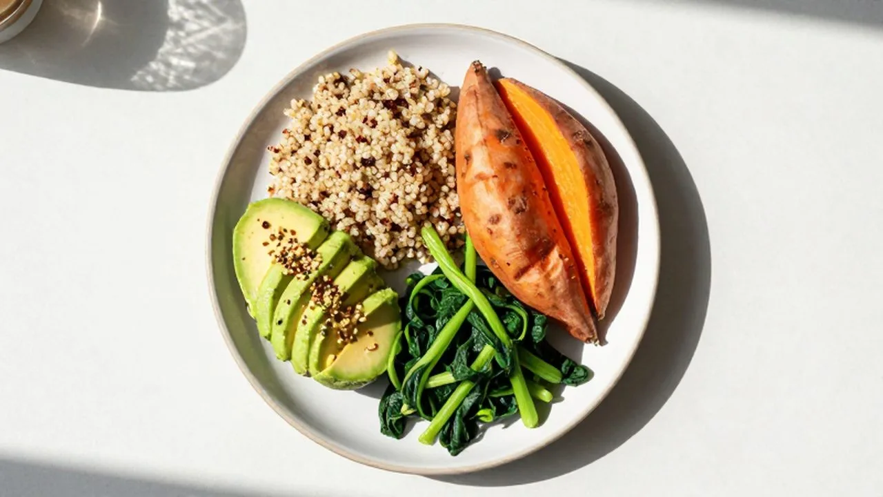 Plato de cerámica con quinoa, batata, aguacate y vegetales verdes bajo luz natural.