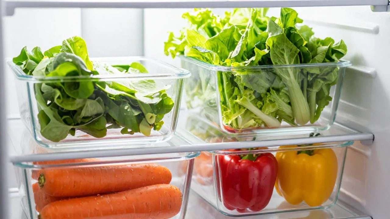Vegetales frescos y coloridos organizados en recipientes de vidrio dentro de un refrigerador limpio.